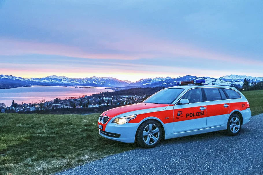 Ein Polizeiauto steht auf einem Parkplatz. Dahinter der Zürichsee in der Ferne.